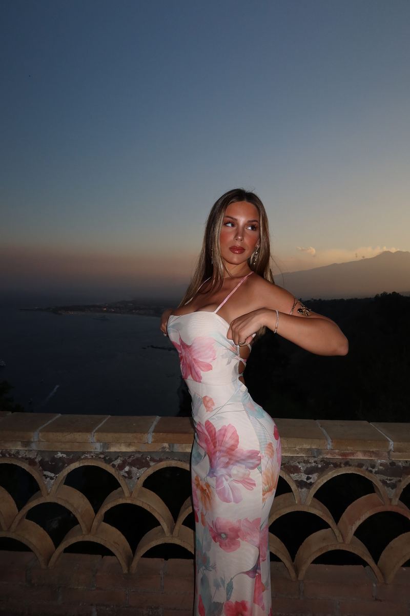 Sara in a floral maxi dress on a terrace above the sea at dusk
